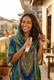 Woman in a colorful patterned dress holding a spray bottle outdoors.